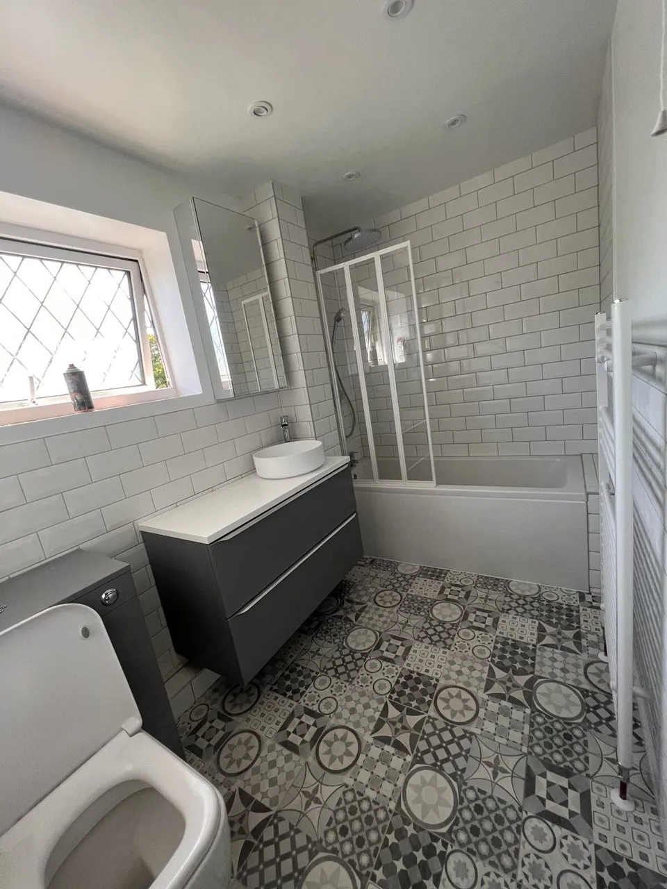 Family bathroom with patterned encaustic-style floor tiles, white metro walls, grey wall-hung vanity and a shower bath, fitted by Basingstoke Bathrooms