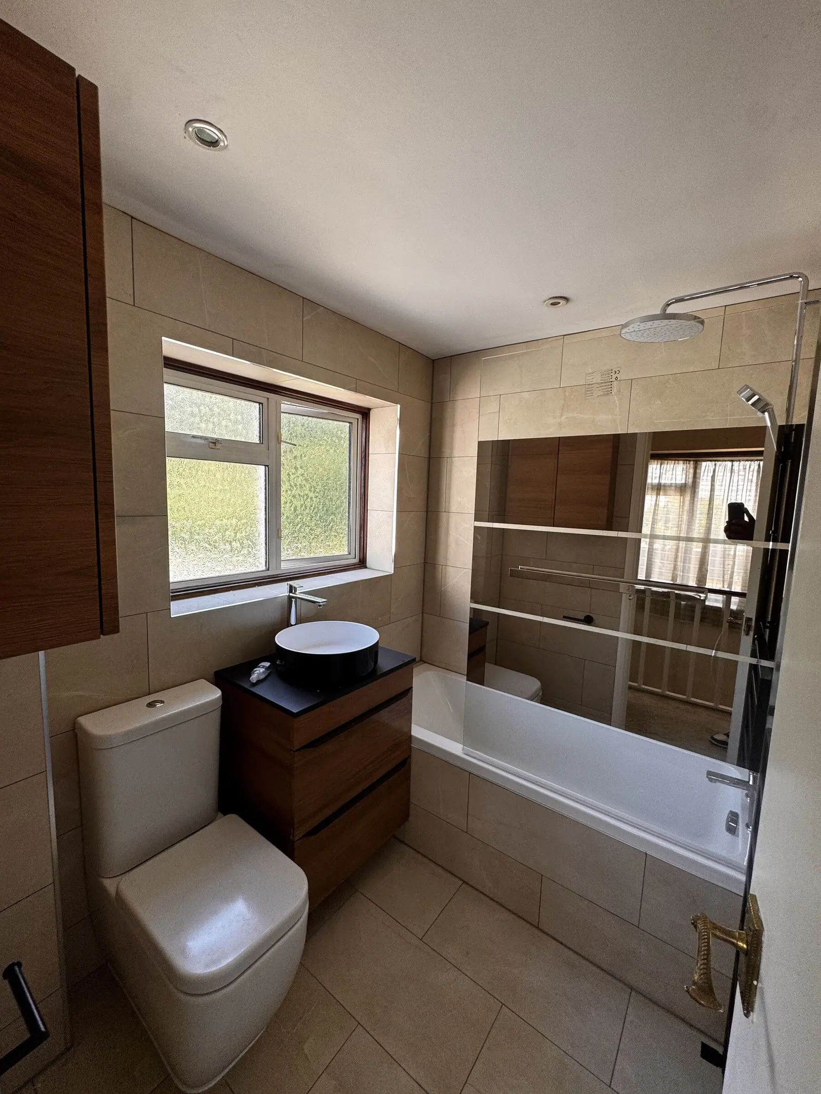Bathroom with a walnut vanity, white vessel basin, beige stone-effect tiles and a bath with black screen, fitted by Basingstoke Bathrooms
