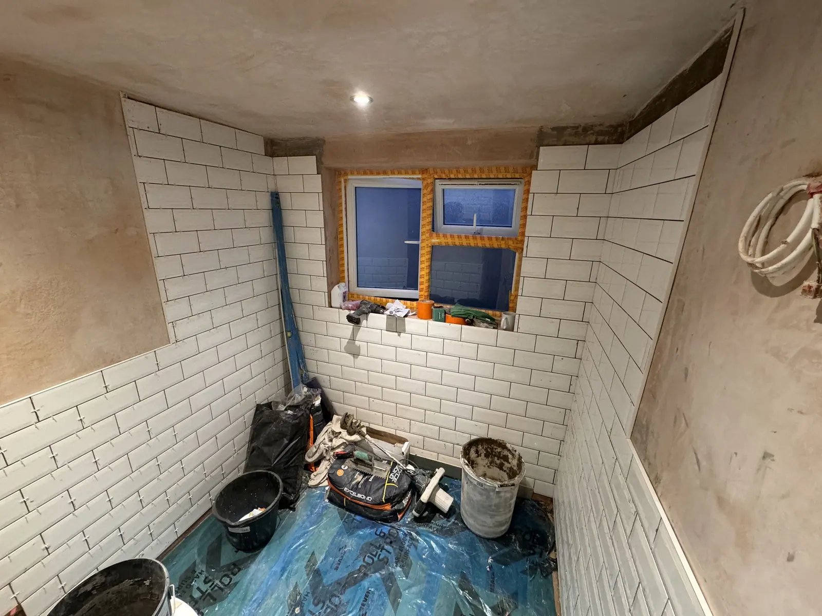 Bathroom part way through: white metro tiles up to half height, walls plastered, pipework at first fix, a Basingstoke Bathrooms job in progress