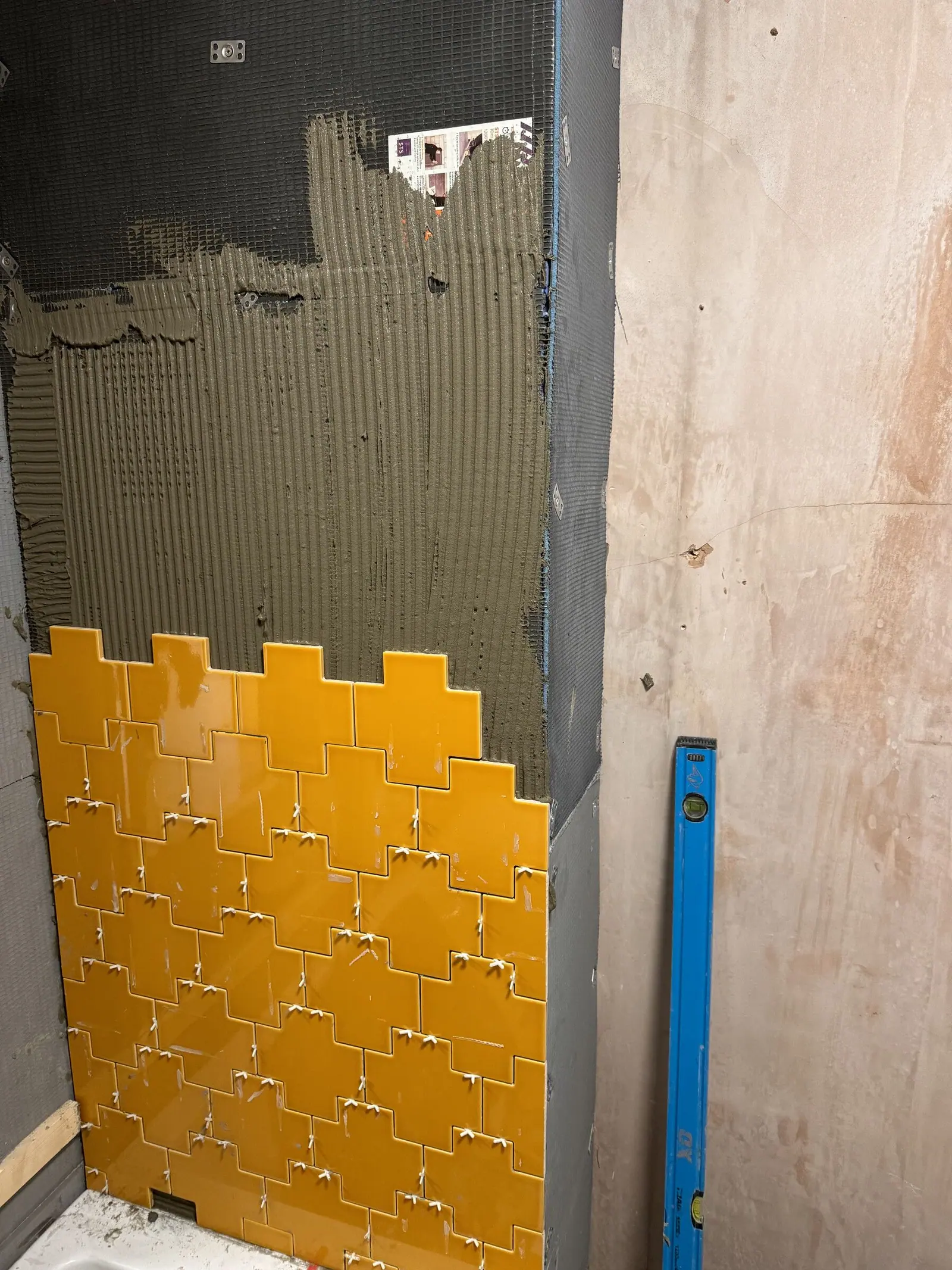 Mustard yellow tiles going onto a tanked wall with spacers in and a spirit level against the board, a Basingstoke Bathrooms job in progress
