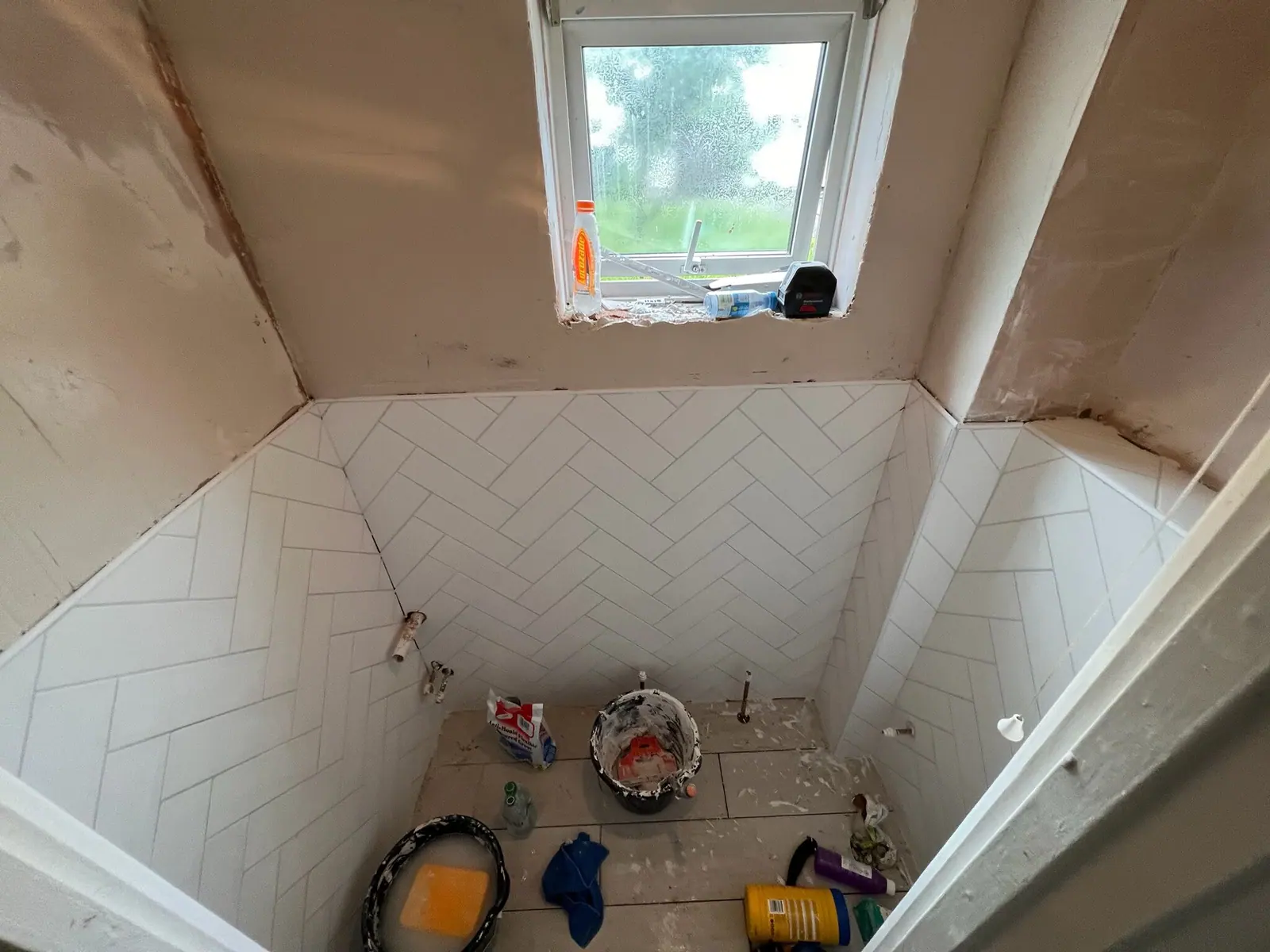 Cloakroom mid-renovation with white herringbone wall tiles going up and the floor still bare, fitted by Basingstoke Bathrooms