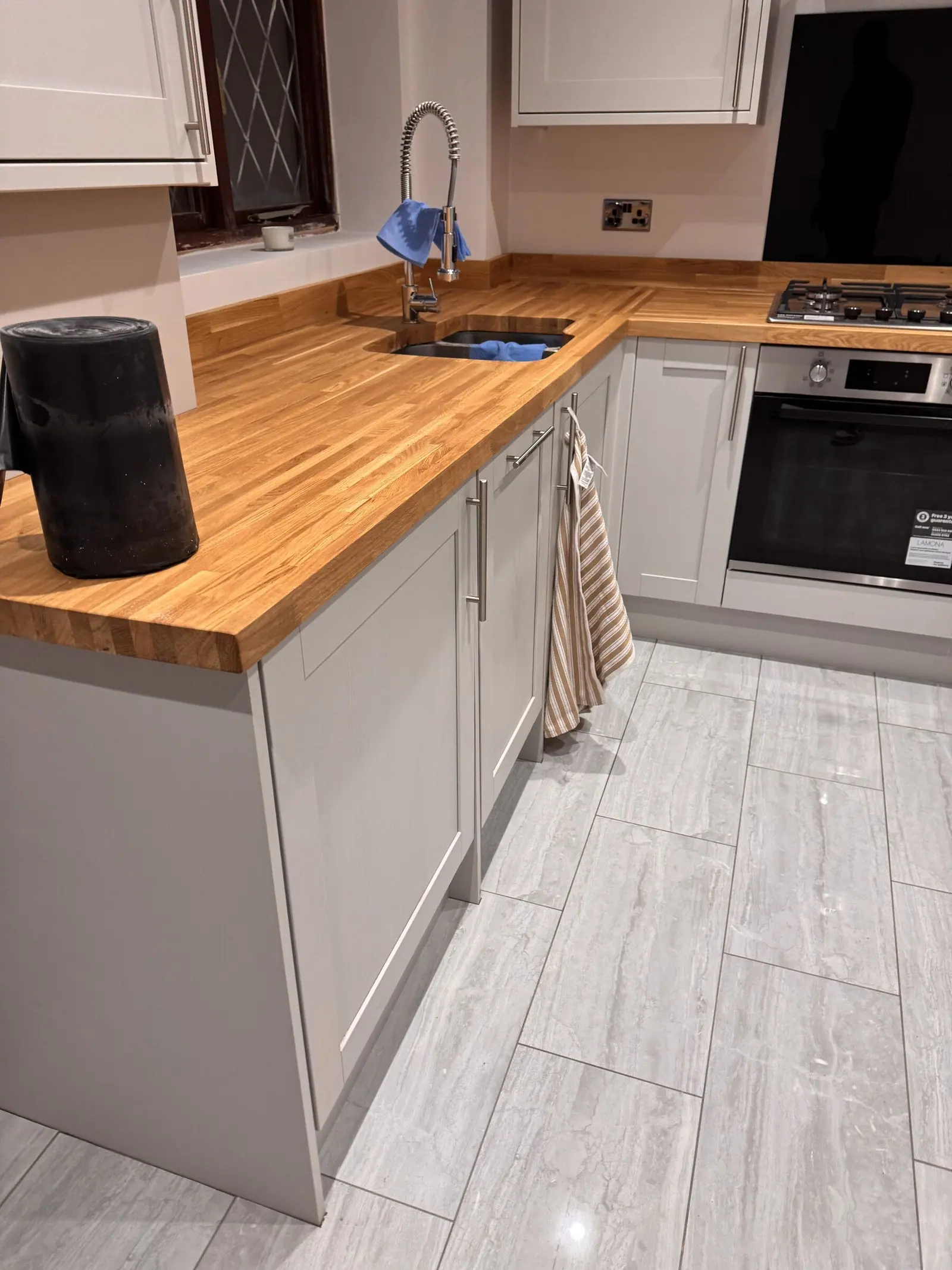 Kitchen with light grey shaker units, solid oak worktops, built-in oven and grey wood-effect floor tiles, fitted by Basingstoke Bathrooms