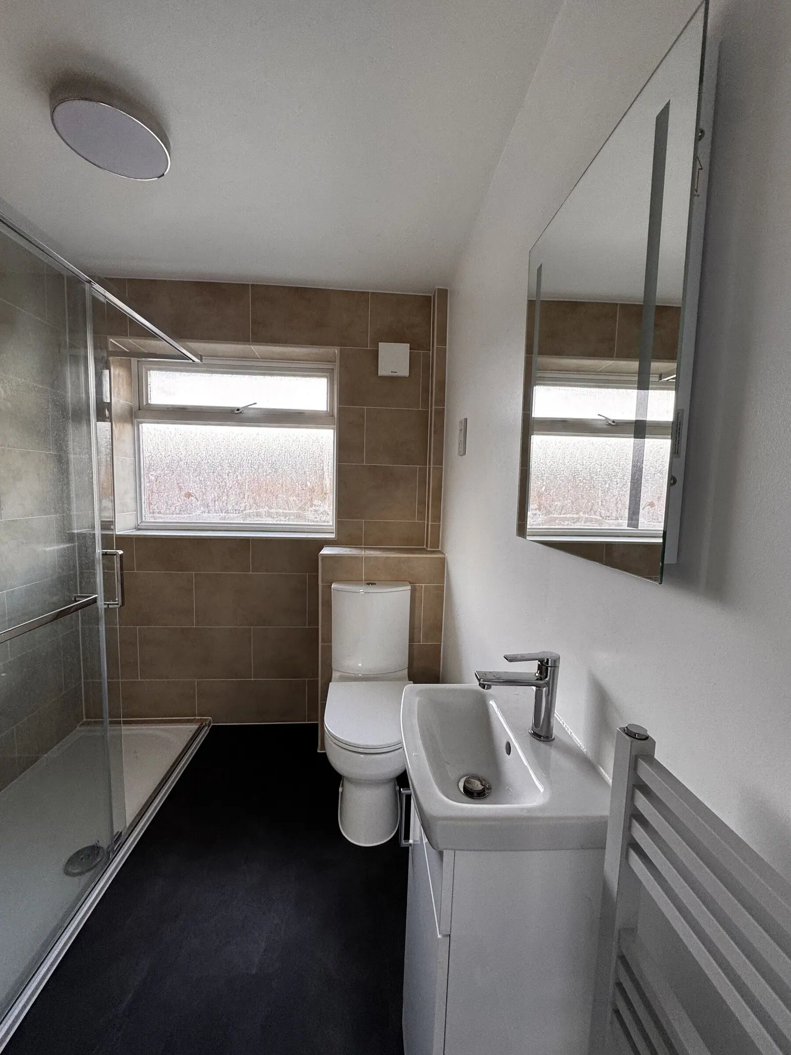 Small shower room with beige tiles, sliding-door shower enclosure, close-coupled WC and compact basin, fitted by Basingstoke Bathrooms