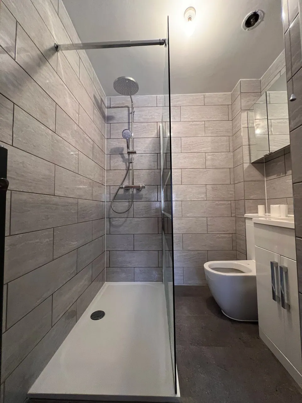 Walk-in shower with grey stone-effect wall tiles, low-profile tray, glass screen and a mirrored cabinet, fitted by Basingstoke Bathrooms