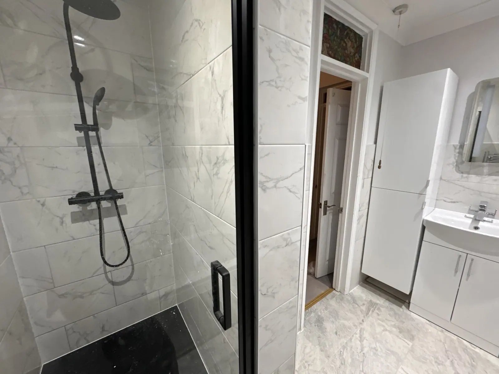 Walk-in shower in marble-effect tiles with matt black thermostatic shower and black-framed screen, fitted by Basingstoke Bathrooms