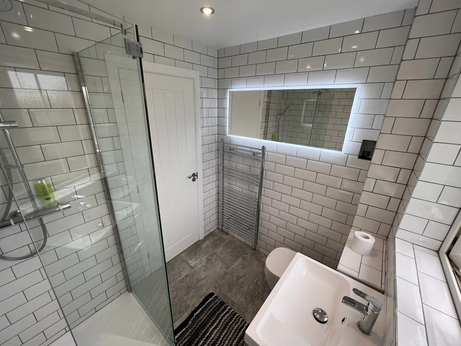 Shower room in white metro tiles with a walk-in shower, frameless screen, LED mirror and grey wood-effect floor, fitted by Basingstoke Bathrooms